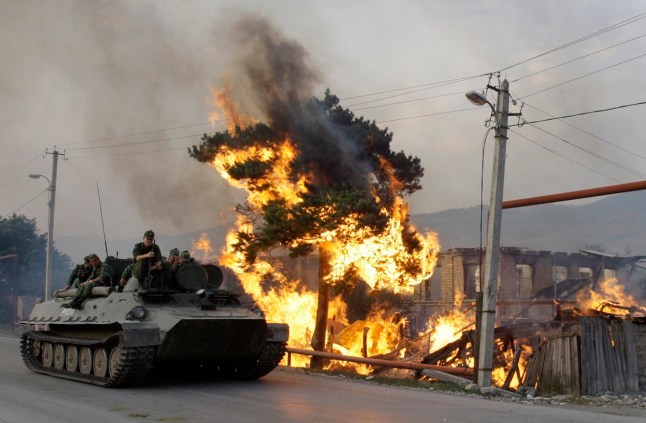 A Russian military vehicle rolls past a house set on fire by South Ossetian militia in the Georgian village of Kvemo-Achebeti outside the South Ossetian capital of Tskhinvali, August 18, 2008. REUTERS/Denis Sinyakov (GEORGIA)